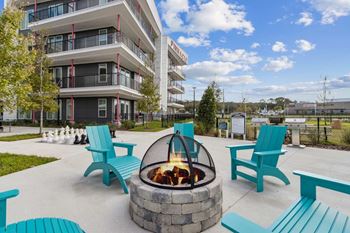 A fire pit sits in the middle of a patio with blue chairs and benches around it.